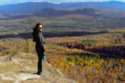 A woman standing on top of an Adirondack Mountains cliff overlooking a New York valley.