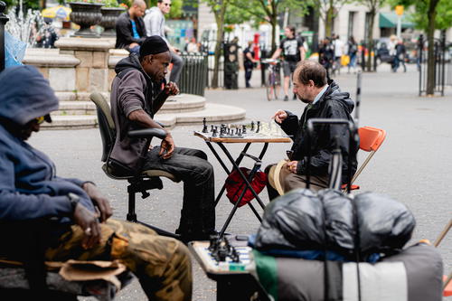 A group of people playing chess on a New York City sidewalk.