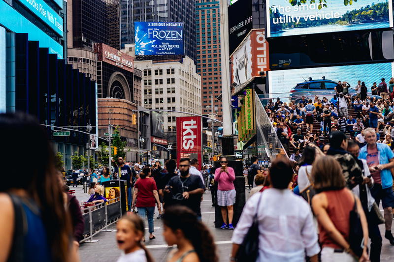 A crowd of people walking down a busy street in NYC's Times Square.
