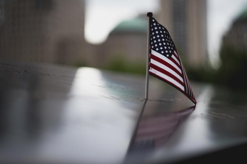A small American flag sits on a table in front of the NYC cityscape.