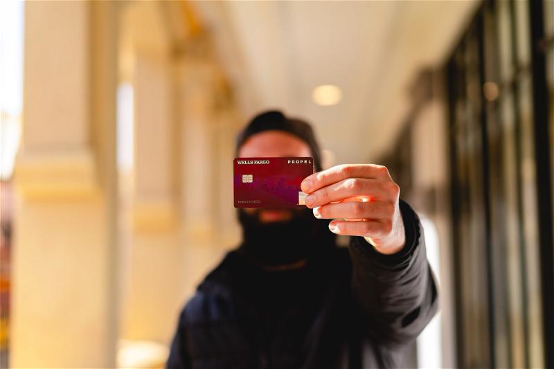 A man holding up a credit card in front of a building in NYC.