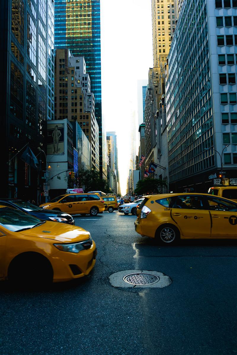 A fleet of NYC yellow taxi cabs lining a bustling city street.