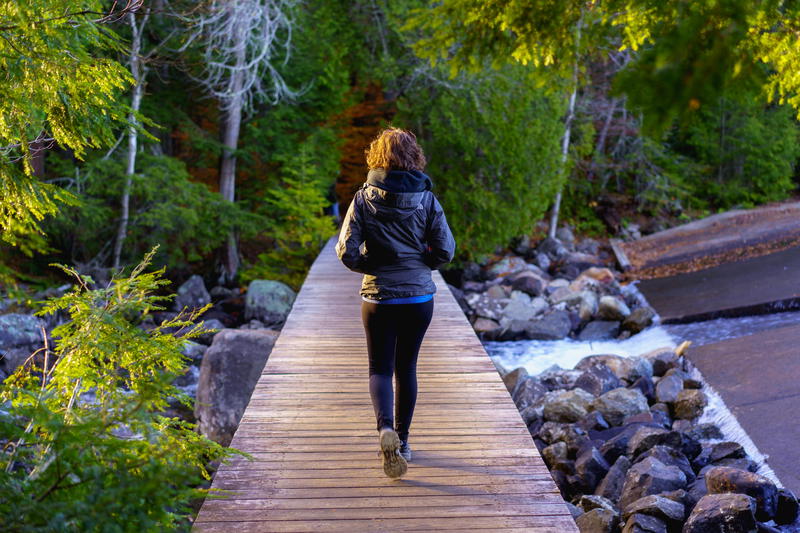 A woman walks across a wooden bridge in the woods of Lake Placid.