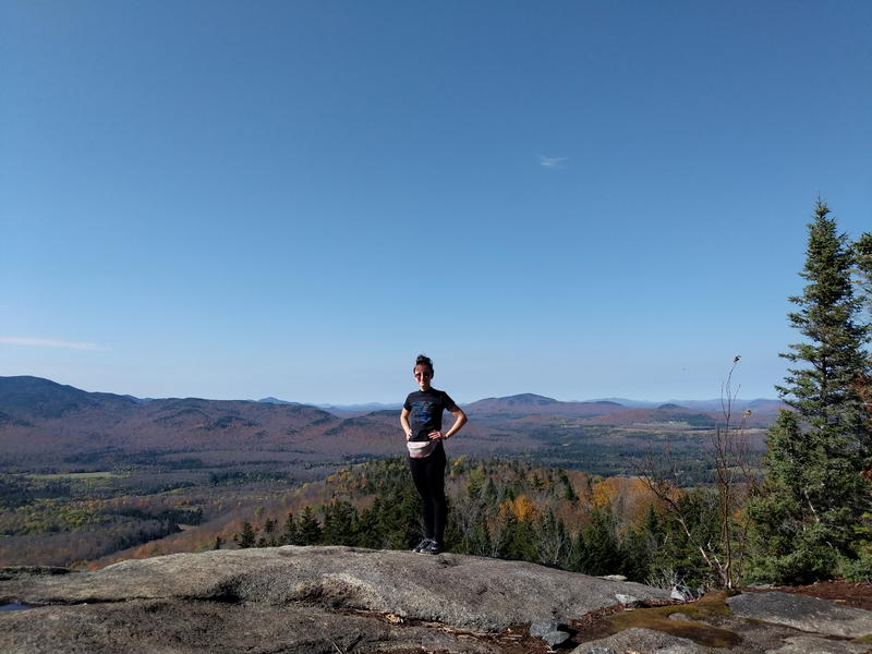 A woman standing on top of a rock with Lake Placid's mountains in the background.