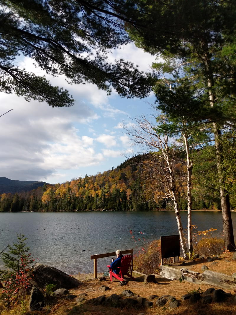 A man sits on a bench next to a lake in Lake Placid.