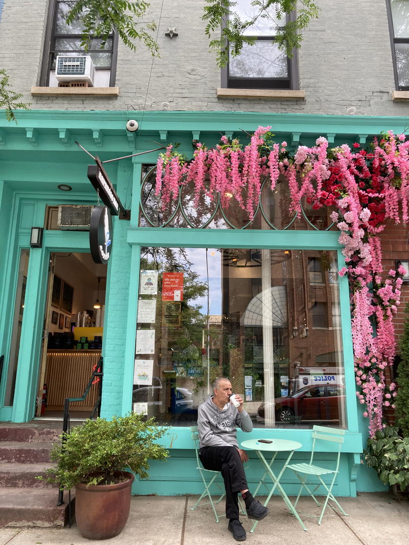 A woman sits at a table in front of a store with flowers in NYC.
