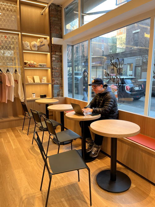 A man sits at a table in a coffee shop in NYC.