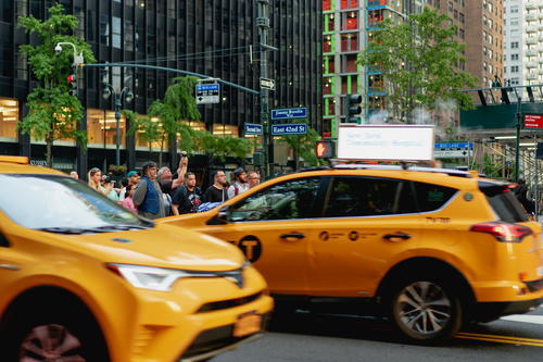 A yellow taxi driving down the street in NYC.