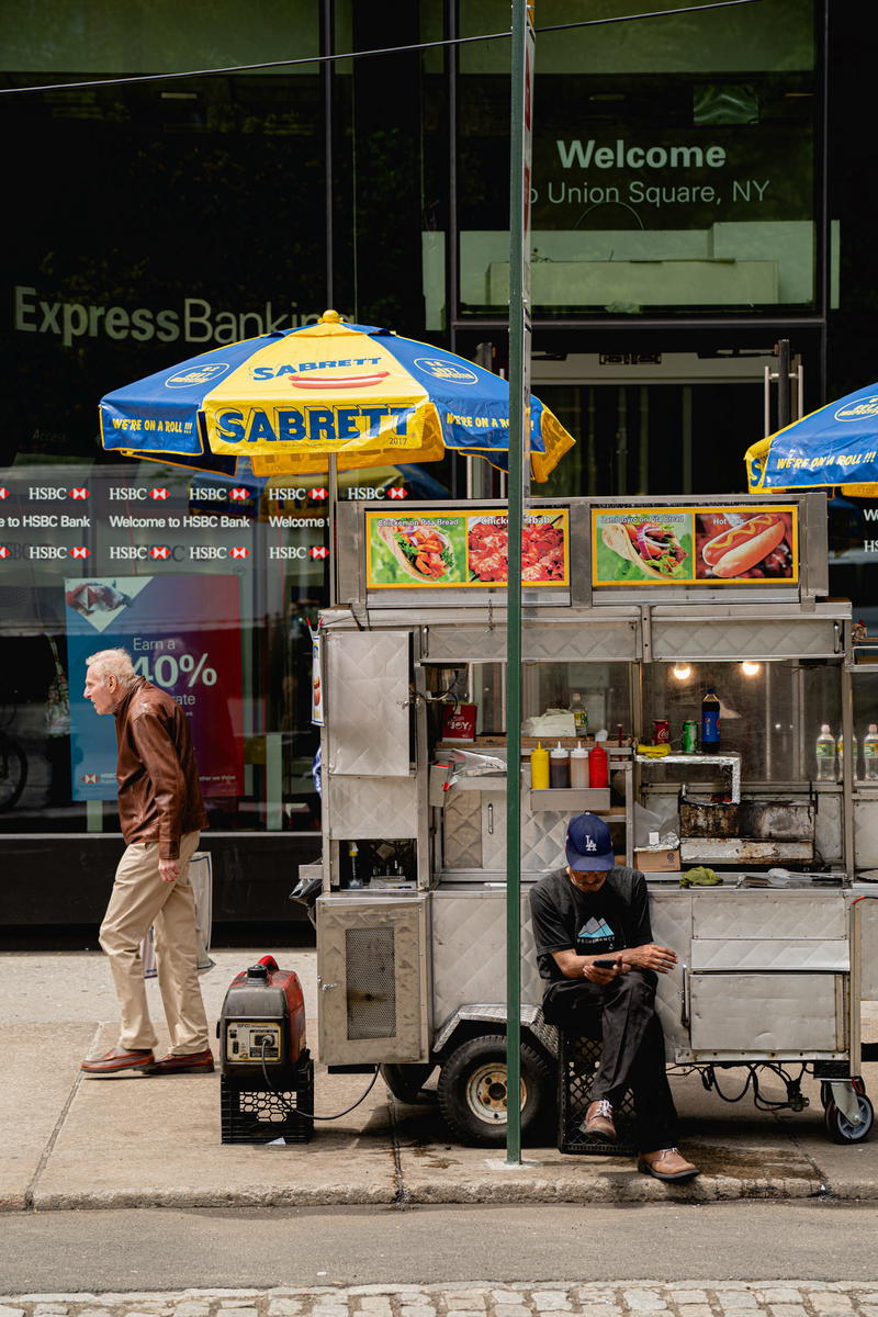 A NYC hot dog cart on a sidewalk.