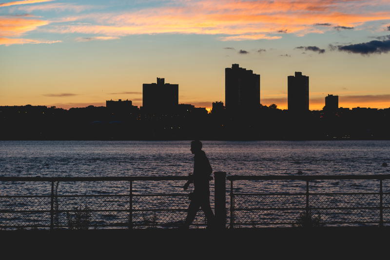 A silhouette of a person walking along the water at sunset in NYC.