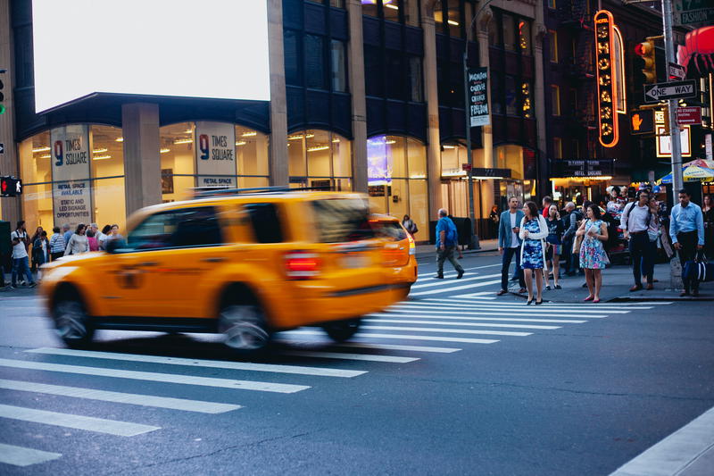 A yellow taxi cab driving down a city street in NYC.