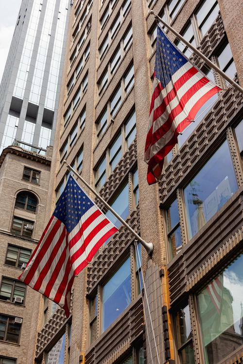 Two American flags fluttering in front of a tall building in NYC.