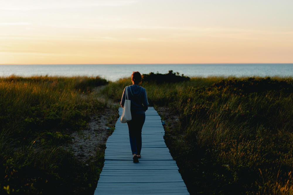 A woman walking down a boardwalk in New York, towards Montauk.