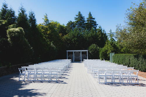 An outdoor ceremony with white chairs and trees in NYC at the New York Botanical Garden.