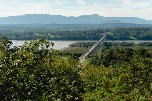 A bridge over a river with trees and mountains in the background at Olana State Historic Site, New York.