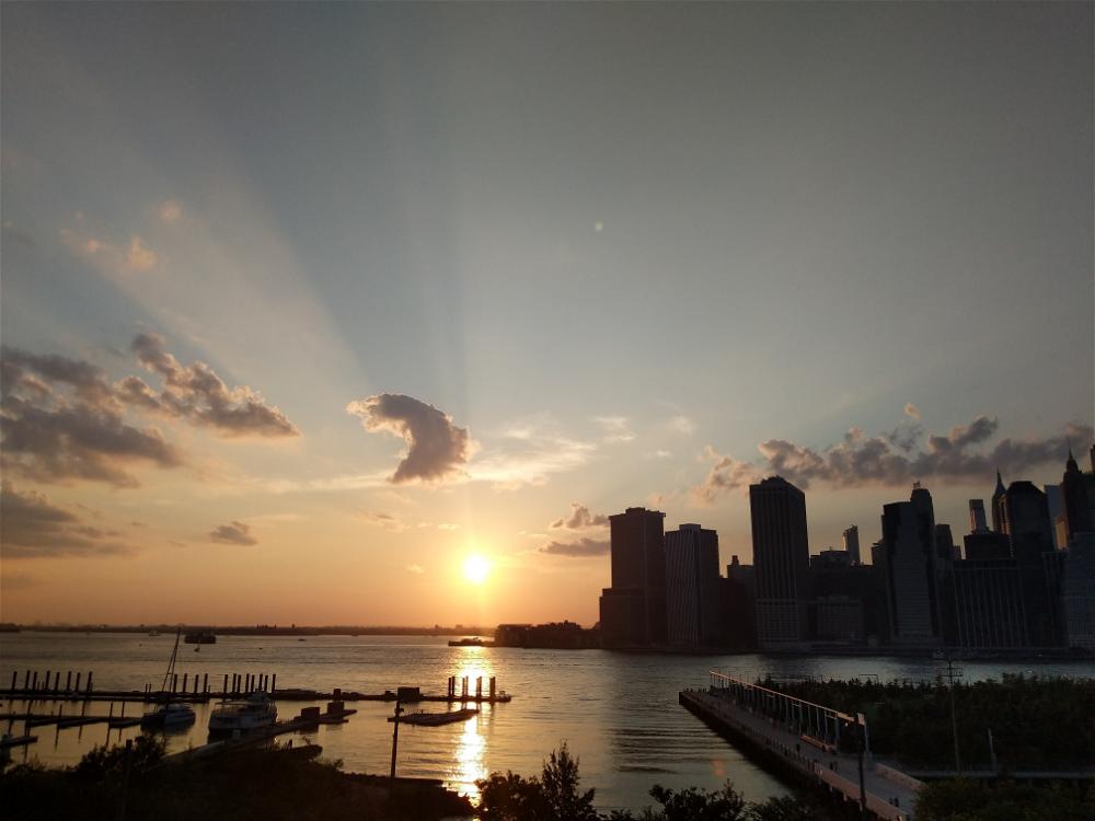 The sun is setting over New York City with a dock.
