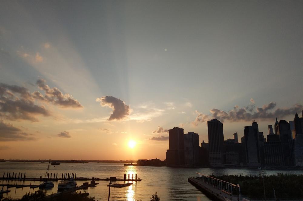 The sun is setting over New York City with a dock.