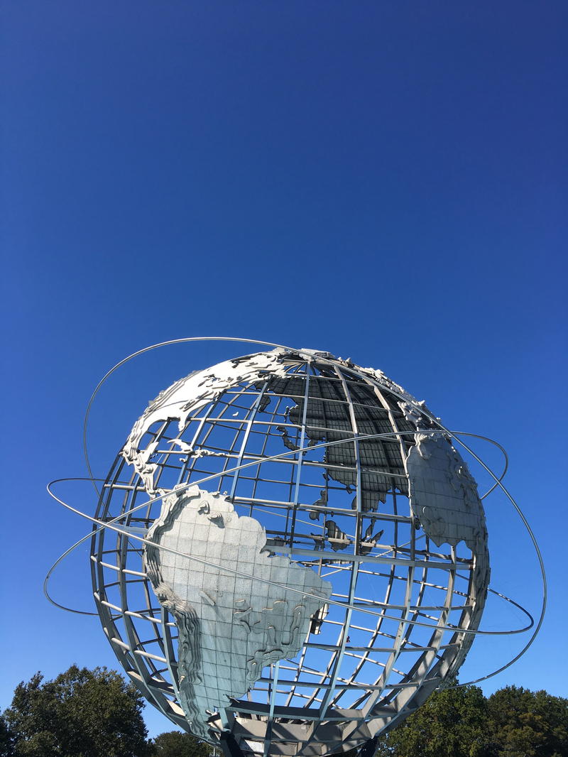 A large metal globe in the middle of a grassy field in NYC.