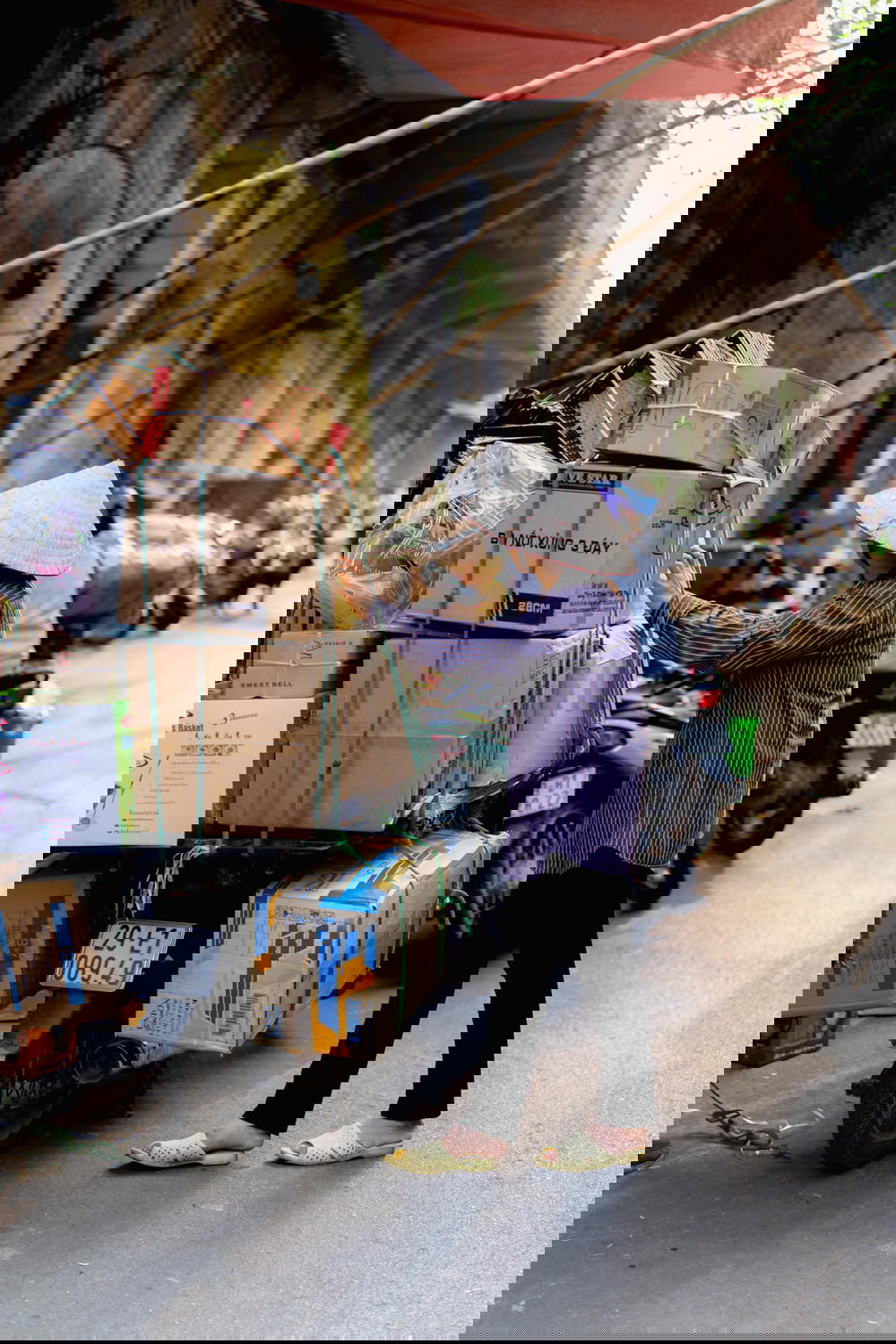 A woman in Hanoi, Vietnam loading boxes onto a motorcycle.