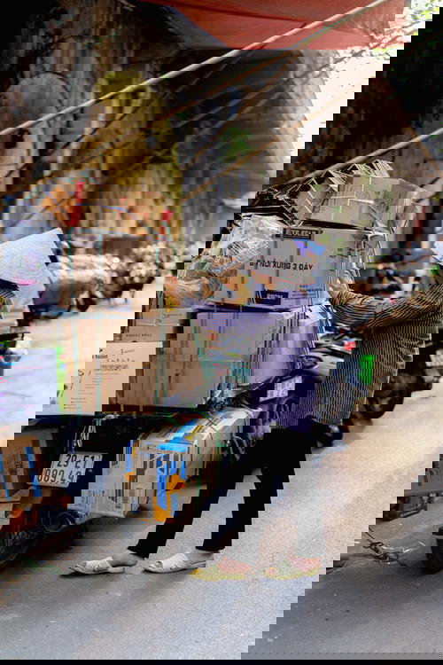 A woman in Hanoi, Vietnam loading boxes onto a motorcycle.