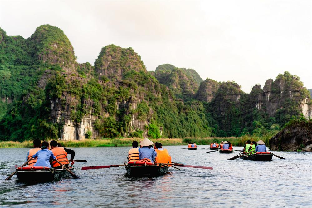 Small rowboats and people in orange life jackets rowing in the river of Tam Coc Vietnam