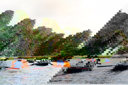 Small rowboats and people in orange life jackets rowing in the river of Tam Coc Vietnam