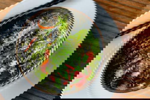 White rice noodles and lettuce shreds in a silver bowl on a white plate with black chopsticks