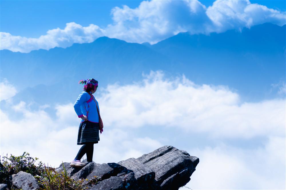 A woman standing on top of a mountain in Sapa, Vietnam, overlooking the clouds.